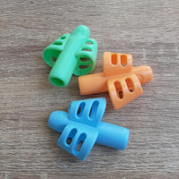 Lot de guides doigts multicolores (vert, orange, bleu), conçus pour améliorer la tenue d’un stylo ou crayon